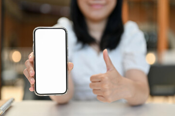 Happy Asian woman showing thumb up and smartphone white screen mockup to camera.