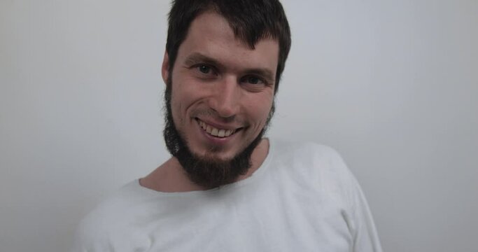Extreme close-up of the face of a violent psychiatric patient. Young caucasian man in straitjacket with beard, dark hair and insane smile looking at the camera in white ward of asulym