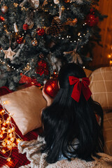 A brunette woman with a red bow in her hair lying near the Christmas tree with festive decorations....
