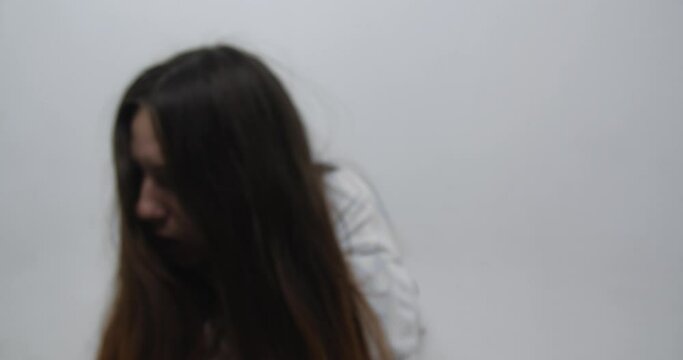 Extreme close up  of teenager girl with   long red hair, dressed in straitjacket, barefoot, tied with straps, sits in the corner of Ward in mental hospital.exacerbation of schizophrenia