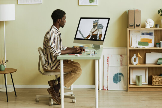 Side view of young creative digital artist sitting in front of computer monitor in studio or at home and drawing digital pictures