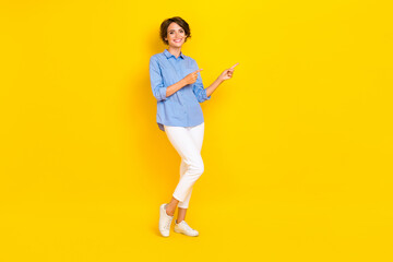 Full length photo of positive pretty lady wear blue shirt pointing two fingers empty space isolated yellow color background
