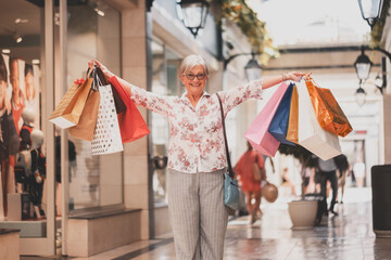 Black friday shopping for attractive smiling senior woman holding shopping bags looking happy at...