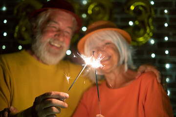 Blurred caucasian senior couple holding sparklers celebrating new year. Happy lifestyle for mature retirees, party lights