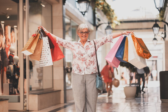 Black friday shopping for attractive smiling senior woman holding shopping bags looking happy at camera, consumerism concept