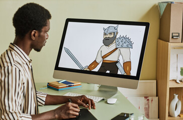 Computer screen with digital artwork being created by young African American male designer sitting by workplace in home office