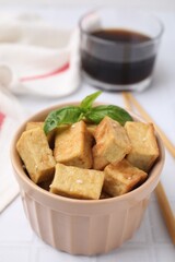 Delicious fried tofu with basil and sesame seeds in bowl on white tiled table