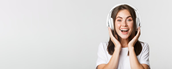 Close-up of smiling attractive brunette girl listening music in headphones, enjoying interesting...