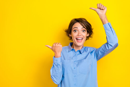 Portrait photo of young funny excited girlish woman wear blue shirt crazy fingers pointing empty space good vacancy isolated on yellow color background