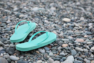Fototapeta na wymiar Stylish turquoise flip flops on pebble seashore. Space for text