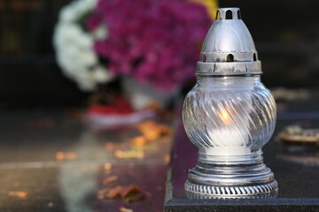 Grave lantern with burning candle on granite surface in cemetery, space for text