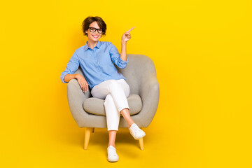 Full length photo of pretty adorable girl dressed blue shirt eyewear relaxing sofa pointing empty...