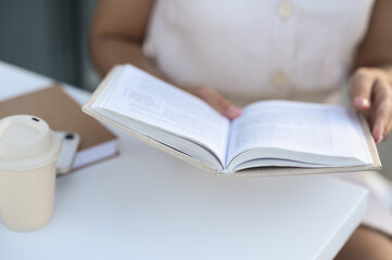 Woman with coffee reading book at white table outdoors, closeup