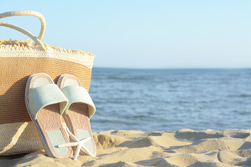 Straw bag, slippers and dry starfish on sandy beach near sea, space for text
