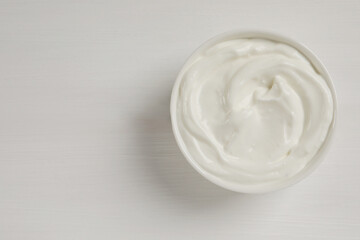 Bowl of fresh yogurt on white wooden table, top view. Space for text