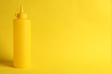 Spicy mustard in plastic bottle on yellow background, space for text