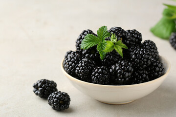 Bowl of fresh blackberries with leaves on white table