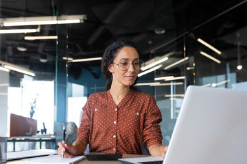 latin american businesswoman working inside office with documents and laptop, worker paperwork calculates financial indicators smiling and happy with success and results of achievement and work