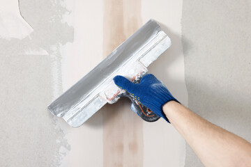 Worker plastering wall with putty knife indoors, closeup