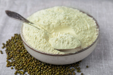 Bowl of flour, spoon and mung beans on light grey cloth, closeup