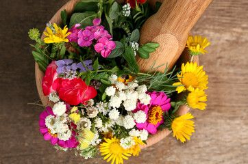 Mortar, pestle and different flowers on wooden table, top view