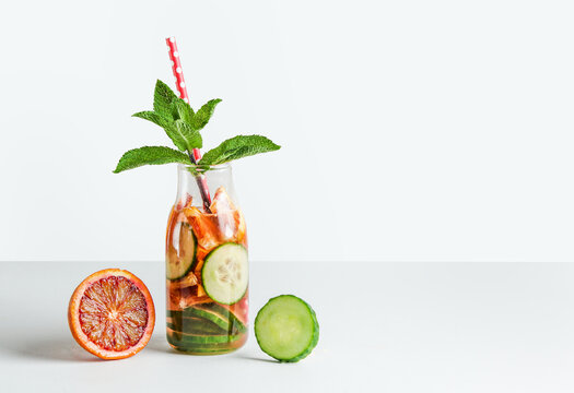Infused watter with fruits and herbs in glass bottle with drinking straw on white table. Healthy drinks concept