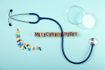 Word Microbes made with wooden cubes, pills and stethoscope on light blue background, flat lay