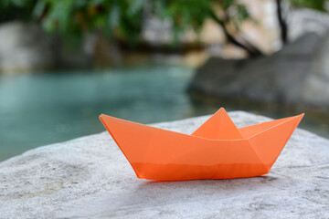 Beautiful orange paper boat on stone near pond, closeup