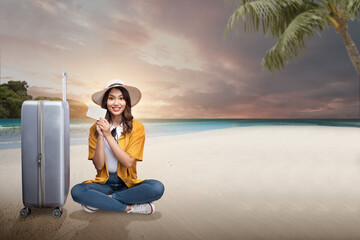 Asian woman with a hat and suitcase sitting while holding empty paper on the beach