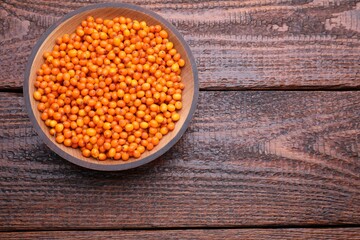 Bowl with fresh ripe sea buckthorn berries on wooden table, top view. Space for text
