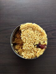 Closeup of onion rice in a stainless steel tiffin, vibrant yellow with red chili bits. The fluffy, well-cooked grains highlight this flavorful, spicy Indian dish.