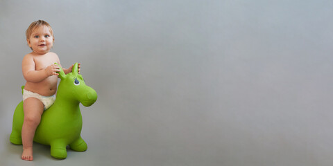 Cute baby riding a rubber horse on a light gray background. A great design for a toy store, a...