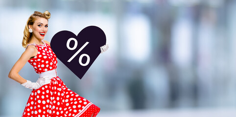 Woman holding paper heart with % sign.  Portrait image of happy pin up girl. Blond model at retro...