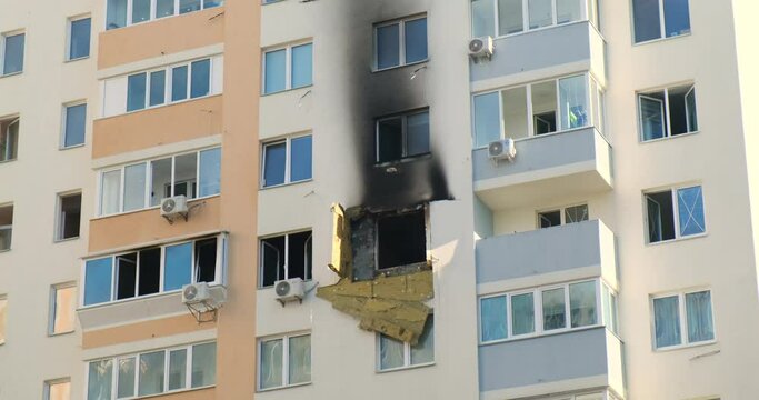 Burnt-out apartment in a high-rise apartment building. Blue sky, windows, air conditioners on the walls. Burnt black window.