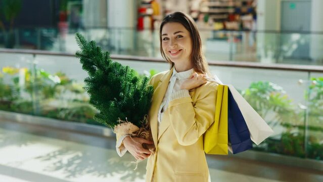Portrait female customer holding xmas tree standing at the shooping mall and looking into the camera. Woman customer getting ready to the celebration of the christmas holidays