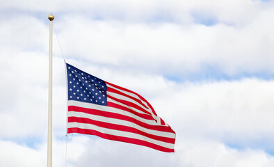 patriotic symbolic representation of an american flag on pole blowing in the wind against cloudy sky with patches of blue