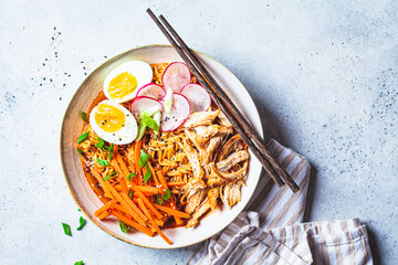 Chicken ramen bowl with carrots, noodles, egg, radish and green onions, gray background. Asian cuisine concept.