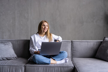 Young woman using laptop while sitting on sofa in living room at home.