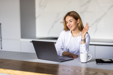 Obraz premium Smiling young woman making video call and heaving a breakfast in her kitchen.