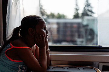 Pensive, wistful little tourist girl in cozy and comfortable train looking out the window, look...