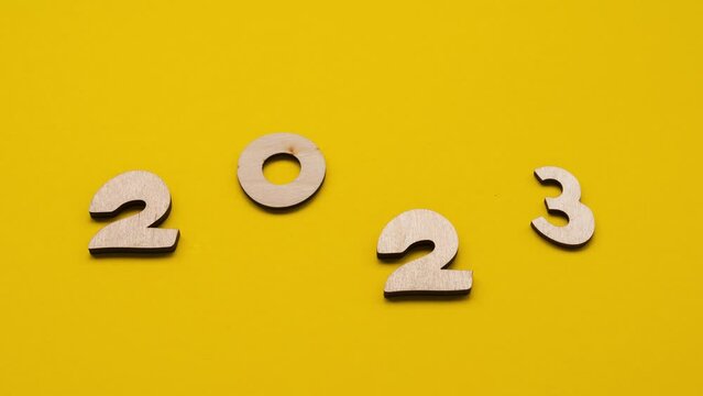 The wooden numbers 2023 appear on a yellow background. The beginning of the new year. Stop motion 4K video