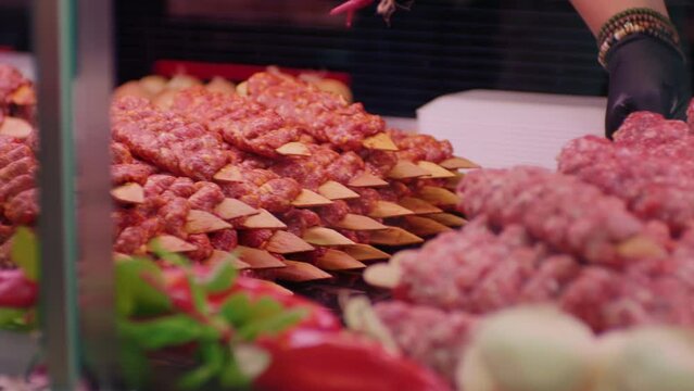Butcher bringing Turkish kebab and barbecue preps on skewers. Fulfilling the gaps with new arrivals. Wooden sticks filled with lamb chunks.