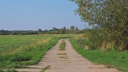 Fototapeta na wymiar Country Road Through Green Fields Paved With Concrete Slabs