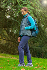 Naklejka na ściany i meble young woman hiker in warm sportswear and with a backpack on a trail near a coniferous forest