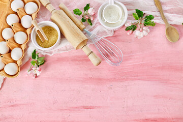 Fototapeta na wymiar Bakery or cooking frame with flowers, ingredients, kitchen items for pastry on pink background, spring cooking theme. Top view, copy space.