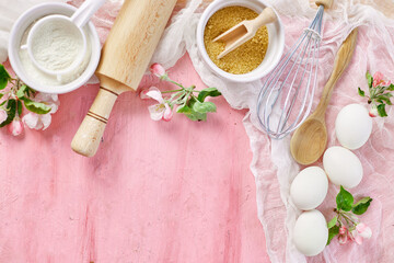 Bakery  or cooking frame with flowers, ingredients, kitchen items for pastry on pink background,  spring cooking theme. Top view, copy space.