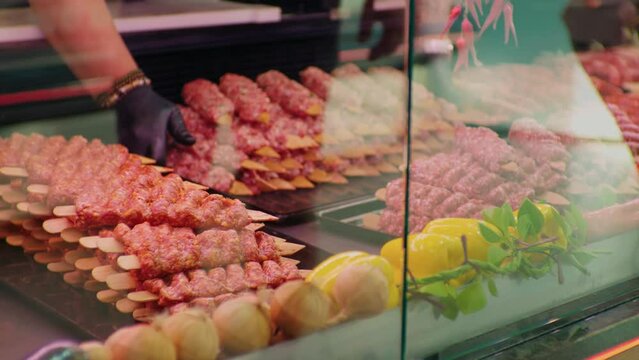 Male hands replacing turkish kebab in the fridge showcase in butchers shop. Butchery worker fulfilling the gaps with precessed meat.