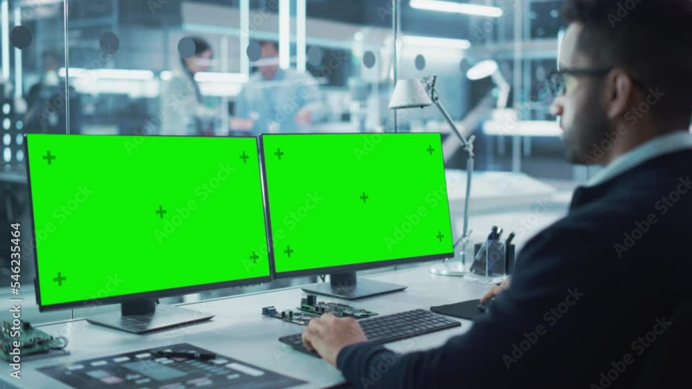 Poster Industrial Engineer Working on a Desktop Computer with Two Green Screen Chromakey Display Screens in a Modern Technological Research and Development Center. Over the Shoulder Shot.