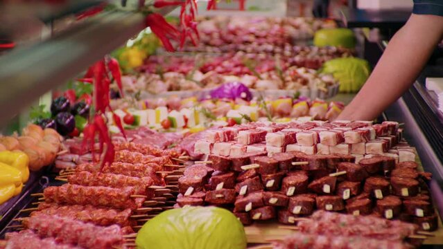 Man hands in gloves placing a tray full of pieces of meat on skewers. Butchery worker fulfilling the gaps with pregessed meat.