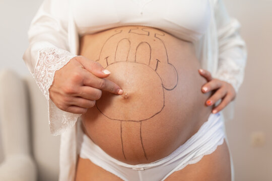 Close up of a pregnant woman's painted belly button while she points at it at home
